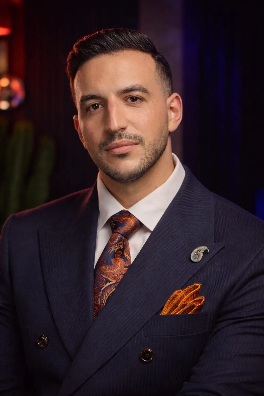 Portrait of Abdollah Mohammadpour in a navy suit with an orange tie