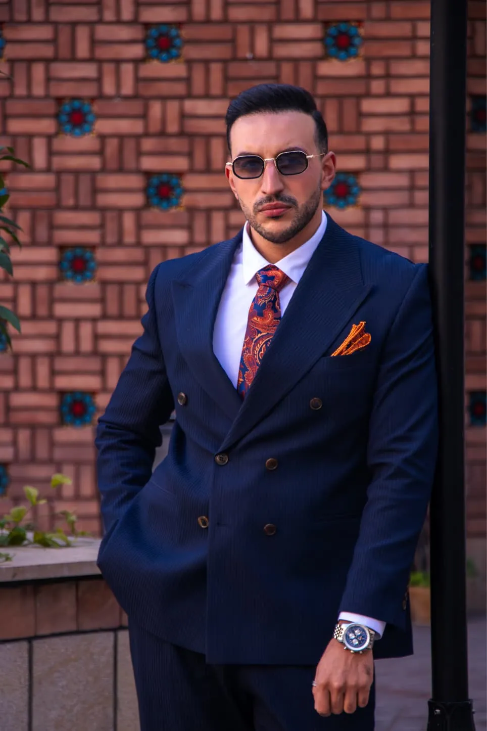 Abdollah Mohammadpour standing in a navy suit with orange tie and pocket square